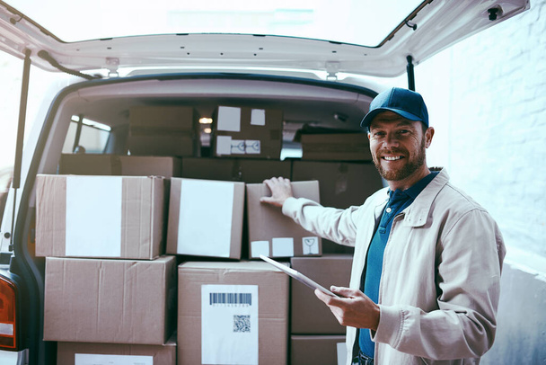 I have a busy day ahead of me. Portrait of a cheerful young delivery man standing next to a van full of boxes while holding a digital tablet - Foto, Imagem