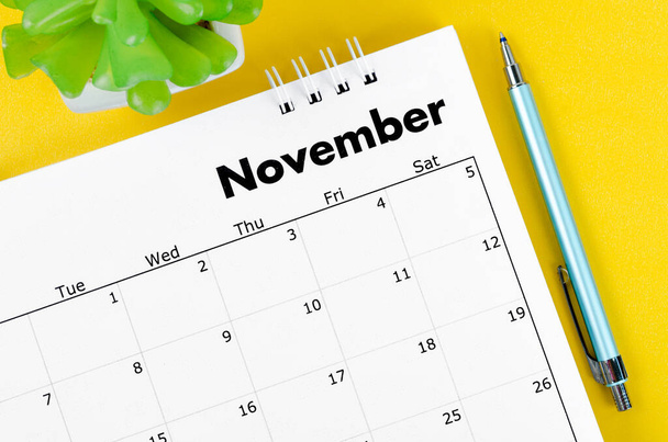 November 2022 desk calendar and pen with plant pot on yellow background. - Valokuva, kuva