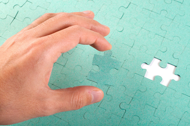 Hand inserting missing piece of green jigsaw puzzle into the hol - Photo, Image