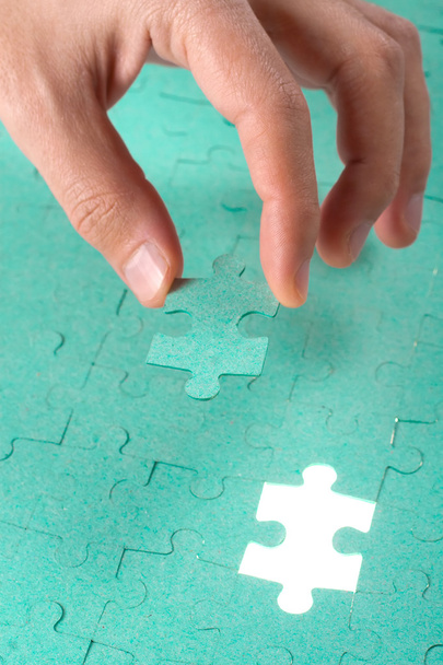 Hand inserting missing piece of green jigsaw puzzle into the hol - Photo, Image