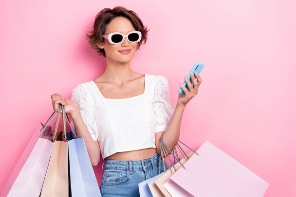 Photo of nice cute lovely girl brunette hair wear white top holding bags smartphone choose dresses online isolated on pink color background. - 写真・画像