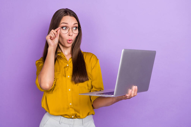 Photo of impressed brown hair lady look laptop wear eyewear brown shirt isolated on purple color background. - Фото, изображение