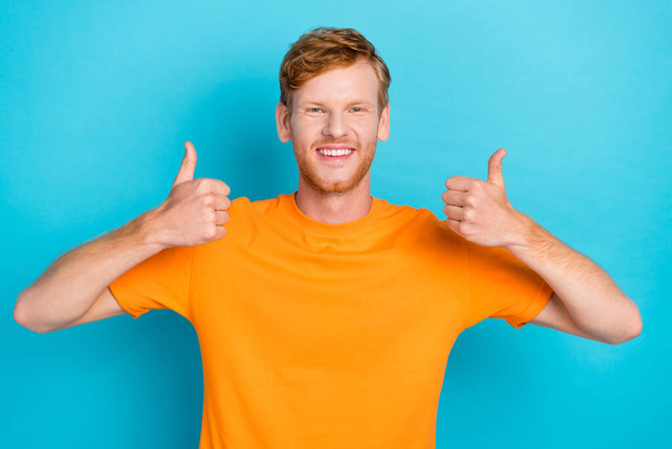 Фотографія оптимістичного веселого красивого чоловіка червоне волосся одягнена помаранчева футболка, що показує великі пальці вгору зворотній зв'язок ізольовано на кольоровому фоні
. - Фото, зображення