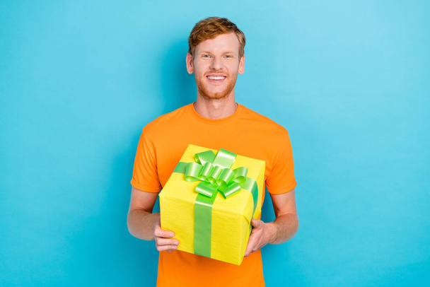 Photo of cute ginger hair guy hold gift wear orange t-shirt isolated on teal color background. - Fotografie, Obrázek