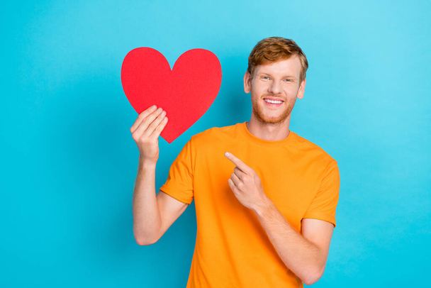 Photo of nice cute boyfriend man toothy smile arm direct index present large red paper love symbol sign isolated on cyan color background. - Foto, immagini