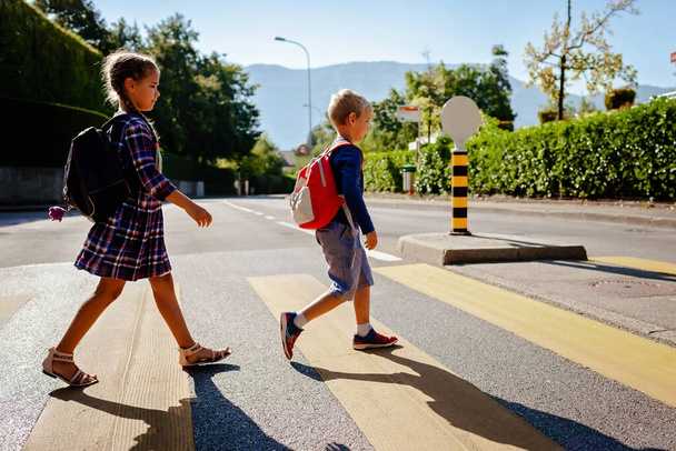 Young pedestrians with backpacks walk to school and cross the road at crosswalk, back to school, school time, child safety, traffic road rules. Study and education concept, lifestyle - Fotoğraf, Görsel