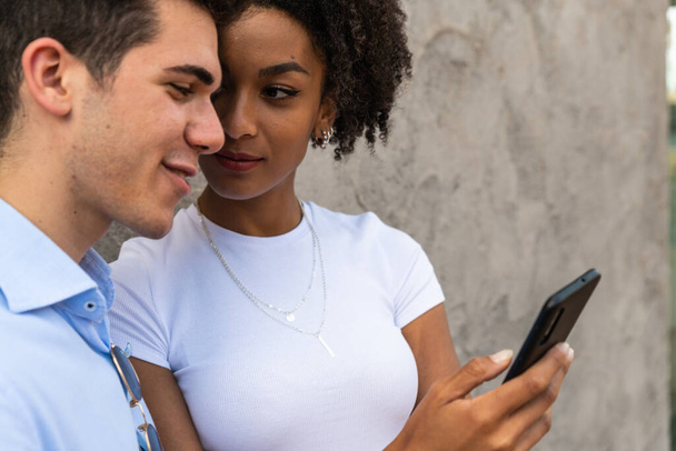 Χαμογελώντας νεαρό ζευγάρι που χρησιμοποιεί το κινητό τηλέφωνο Ευτυχισμένοι νέοι άνθρωποι που αναζητούν smartphone χαμογελώντας γυναίκα και ο άνθρωπος φαίνονται κινητό τηλέφωνο  - Φωτογραφία, εικόνα