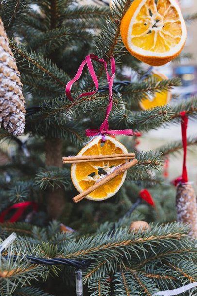 Φυσική διακόσμηση από φέτες πορτοκαλιού και χριστουγεννιάτικα μπαχαρικά σε κορδέλα σε χριστουγεννιάτικο δέντρο. Χριστουγεννιάτικη διακόσμηση. Περιβάλλον, ανακύκλωση, επαναχρησιμοποίηση και μηδενική έννοια των αποβλήτων. Επιλεκτική εστίαση - Φωτογραφία, εικόνα