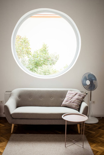 grey sofa in cozy living room with round window - 写真・画像