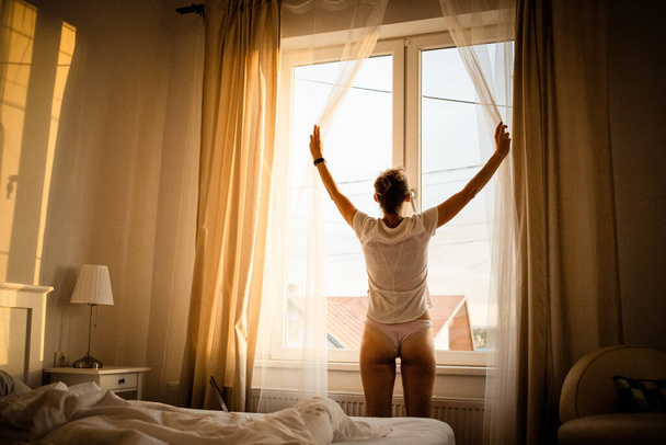 женщина, открывающая занавески спальни на ярком восходе солнца - Фото, изображение