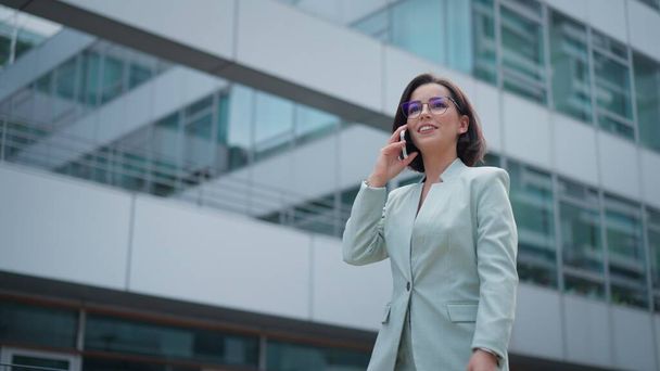 Cute businesswoman having conversation on smartphone outdoors. Portrait of beautiful caucasian female business person who talking on cell phone dressed green suit standing city street - Foto, Bild