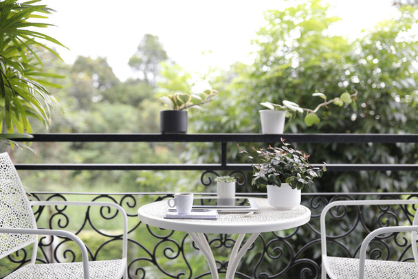 Кавова чашка і планшет і горщик для рослин на білому металевому столі на відкритому повітрі
 - Фото, зображення