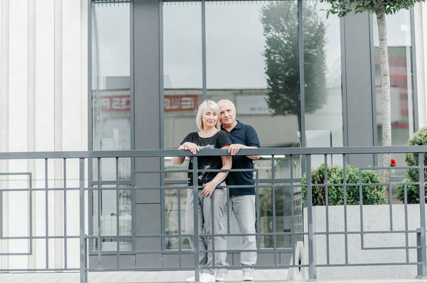 a woman and a man embrace near a glass building - Foto, imagen