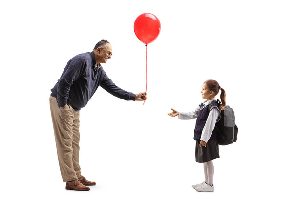 Full length profile shot of a mature man giving a red balloon to a schoolgirl isolated on white background - Foto, Imagem
