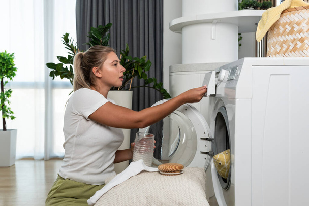 Young woman or housewife putting clothes and laundry to the washing machine to wash the stuff to be clean and fresh. Girl work as a maid to pay her college bills washing laundry. - Foto, immagini