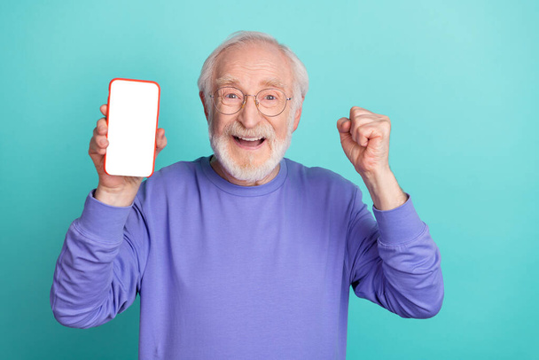 Photo of funny delighted person raise fist celebrate achievement empty space phone screen isolated on cyan color background. - Photo, image