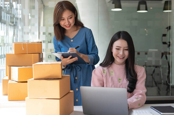 Portrait of Starting small businesses SME owners, two Asian woman check online orders Selling products working with boxs freelance work at home office, sme business online small medium enterpris - Fotó, kép