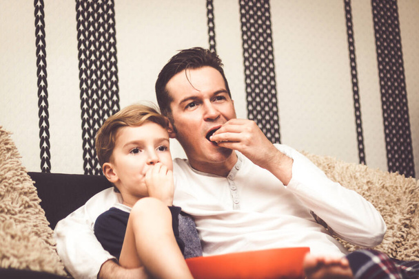 Отец и сын едят попкорн и отдыхают вместе во время просмотра фильма вечером.  - Фото, изображение