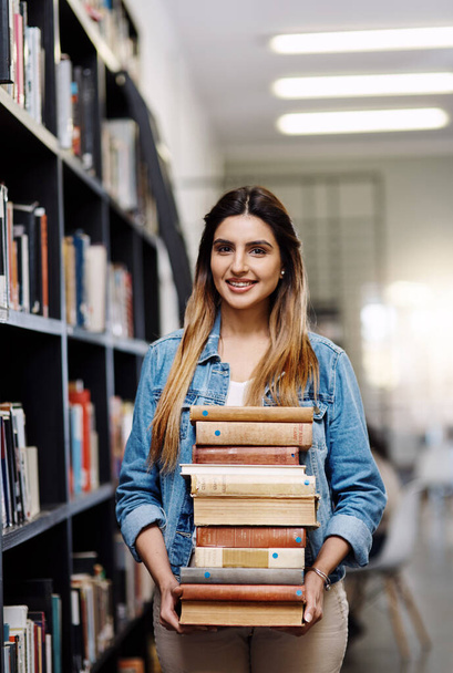 These are all the books Ill need this academic year. Portrait of a happy young woman carrying books in a library at college - Фото, изображение