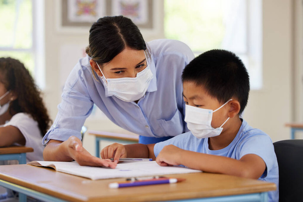 Covid, students and education teacher helping learning children in school classroom to answer math question. Woman with face mask teaching asian boy in lesson with diverse class of kids or classmates. - Zdjęcie, obraz