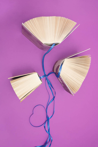 Old books and blue ribbons on bright purple background. Education, knowledge or nature concept. Flat lay. For book lovers. - Photo, Image