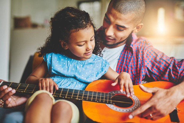 Whats passion if you cant share it. an adorable little girl and her father playing a guitar together on the sofa at home - Foto, immagini