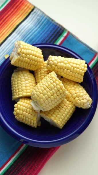 Голубая тарелка с кусками кукурузного початка на цветной скатерти. Вертикальное видео. - Кадры, видео
