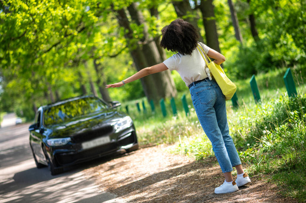 Hitchhiking. Curly-haired young girl hitchhiking and looking excited - Foto, Bild