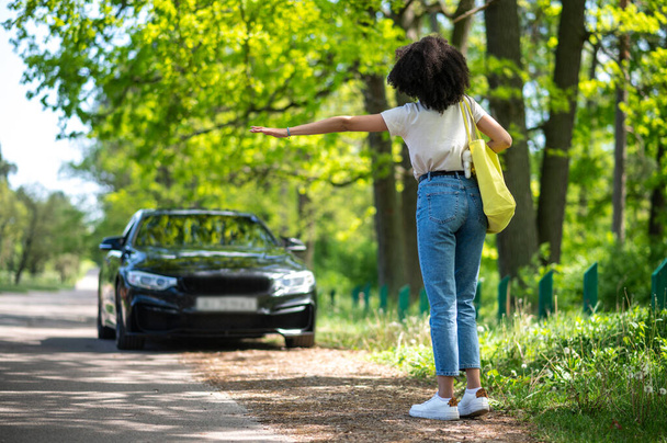 Girl on the road. Curly-haired slim young woman stopping the car in the park - Fotó, kép
