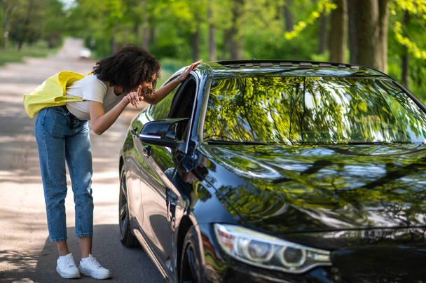 Girl on the road. Curly-haired slim young woman stopping the car in the park - Foto, Imagen