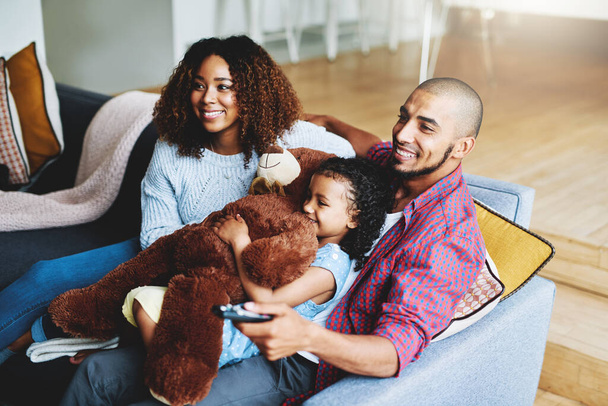 Наконец-то нашли отличное семейное шоу. счастливая молодая семья из трех человек смотрит телевизор вместе в своей гостиной дома - Фото, изображение