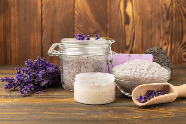 Lavender spa. Sea salt, lavender flowers, essential oils, body cream and handmade soap. Natural herbal cosmetics with lavender flowers on brown texture background. Relax and spa concept. Space for text. - Photo, Image