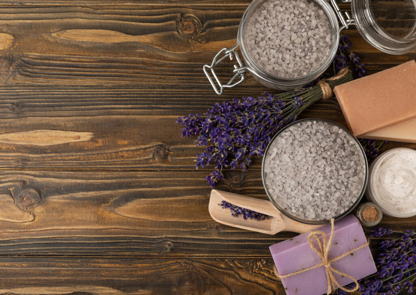 Lavender spa. Sea salt, lavender flowers, essential oils, body cream and handmade soap. Natural herbal cosmetics with lavender flowers on brown texture background. Relax and spa concept. Space for text. - Foto, Bild