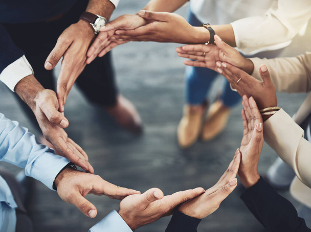 Our strength is connected and forms a circle. Closeup of a group of unrecognizable businesspeople holding hands in a certain way to form a circle inside of the office - Foto, Imagen