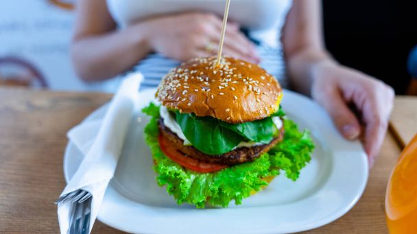 Vegetarian hamburger healthy vegan burger. Cute cheerful girl eating veggie sandwich with salad, avocado, vegetable. Vegan burger healthy diet food - 写真・画像