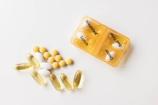 Medicine dispenser. Plastic daily box part of seven day weekly container with different white and yellow pills on white background. Top view, copy space - 写真・画像
