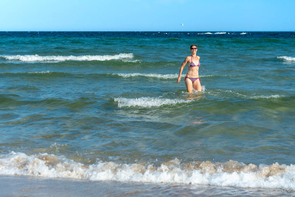 Привлекательная коротковолосая женщина в возрасте тридцати лет в бикини, стоящая в синем море с раскинутыми руками в солнечный летний день. Мбаппе для отдыха, расслабления, психического здоровья, радости - Фото, изображение