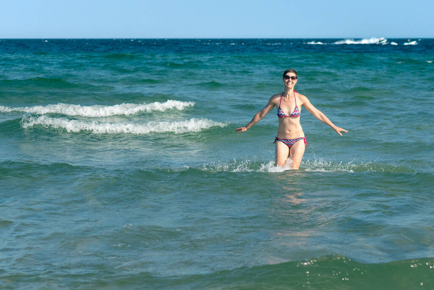 Attractive sporty short haired woman in her thirties, wearing bikini, standing in the blue sea with her arms spread on a sunny summer day. Concept for holiday, vacation, relaxation, mental health,joy - Foto, Bild