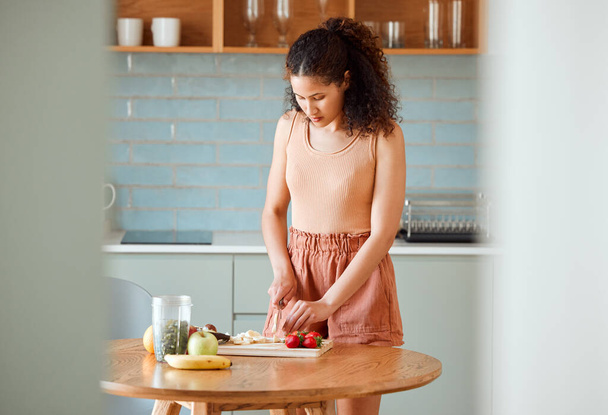 Health, meal and healthy woman alone preparing a nutritional breakfast for herself in the kitchen. Female cutting fruit to make a smoothie or salad with nutrition for an organic lifestyle at home - 写真・画像