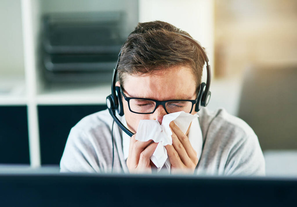 Hope Im not getting sick again. a young call centre agent blowing his nose while working in an office - Foto, imagen