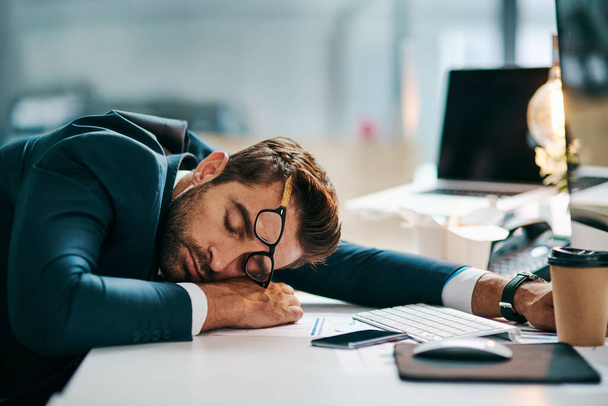 He is one hard working guy. a tired young businessman sleeping on his desk inside of the office during the day - 写真・画像