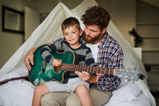 Я вчуся грати на гітарі. Обрізаний портрет чарівного хлопчика, який сидить на колінах своїх татів, навчаючись грати на гітарі вдома
 - Фото, зображення