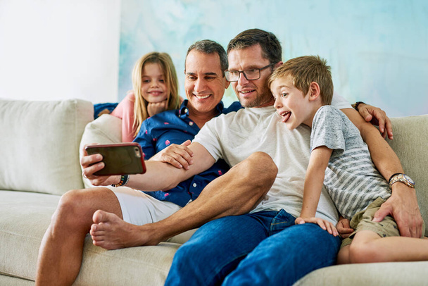 Οικογενειακή διασκέδαση. στοργική τετραμελής οικογένεια που βγάζει selfies στον καναπέ στο σπίτι - Φωτογραφία, εικόνα