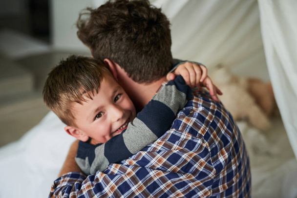 Я люблю свого батька. Портрет чудового маленького хлопчика, який обіймає батька в своїй спальні вдома
 - Фото, зображення
