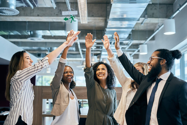 Lets put them up team. a group of cheerful young businesspeople stretching out their hands for a high five after a meeting in the office at work - Foto, immagini