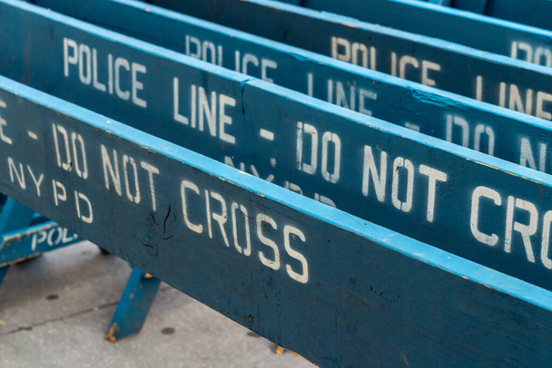 Close up view of several weathered and worn blue wooden road barricades with NYPD Police line do not cross written on them as they sit on a concrete sidewalk. - Zdjęcie, obraz