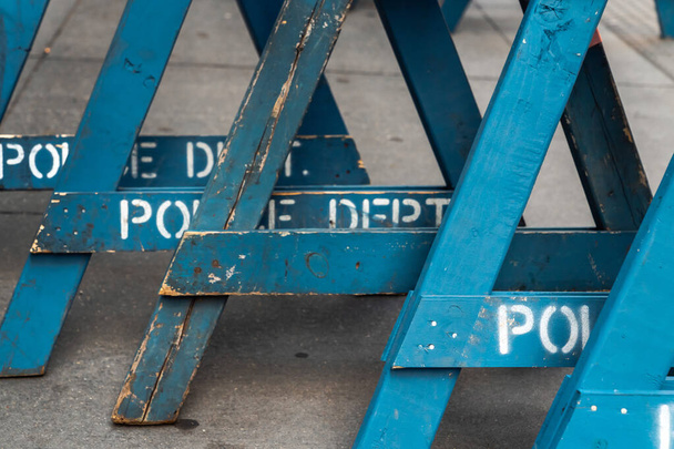 Close up view of several stacked weathered and worn blue wooden road barricade A-frame legs with Police Department written on them as they sit on a concrete sidewalk in New York City. - Foto, Bild