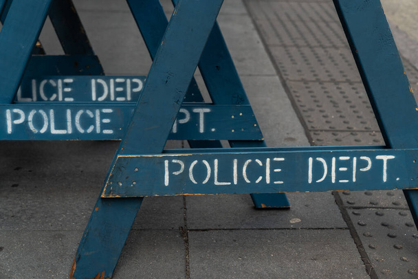 Close up view of several stacked weathered and worn blue wooden road barricade A-frame legs with Police Department written on them as they sit on a concrete sidewalk in New York City. - Foto, afbeelding