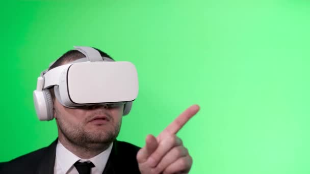A man in a black suit uses virtual reality goggles. VR. Green background. The office worker uses a virtual interface. Movement of hands on a green background chromakey. - Footage, Video