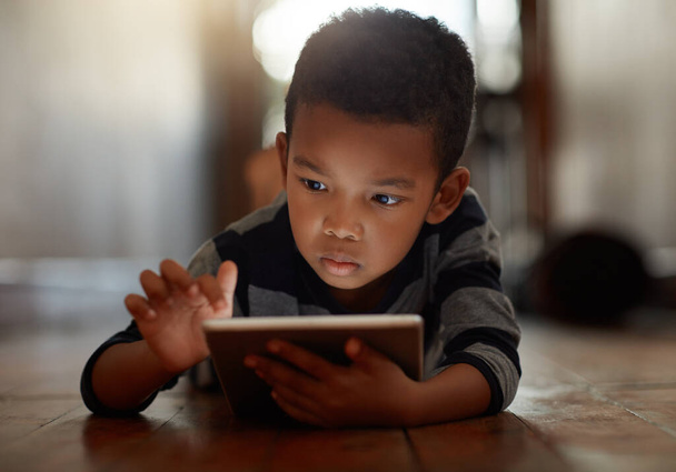 Дети в наши дни технически подкованы. мальчик использует свой цифровой планшет, лежа на полу дома - Фото, изображение